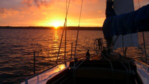 Een zeilboot bij zonsondergang met een helder uitzicht op de horizon en rustig water.