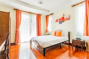 Une chambre avec un plancher en bois, un lit avec une literie blanche, des rideaux orange et un tableau accroché au mur.