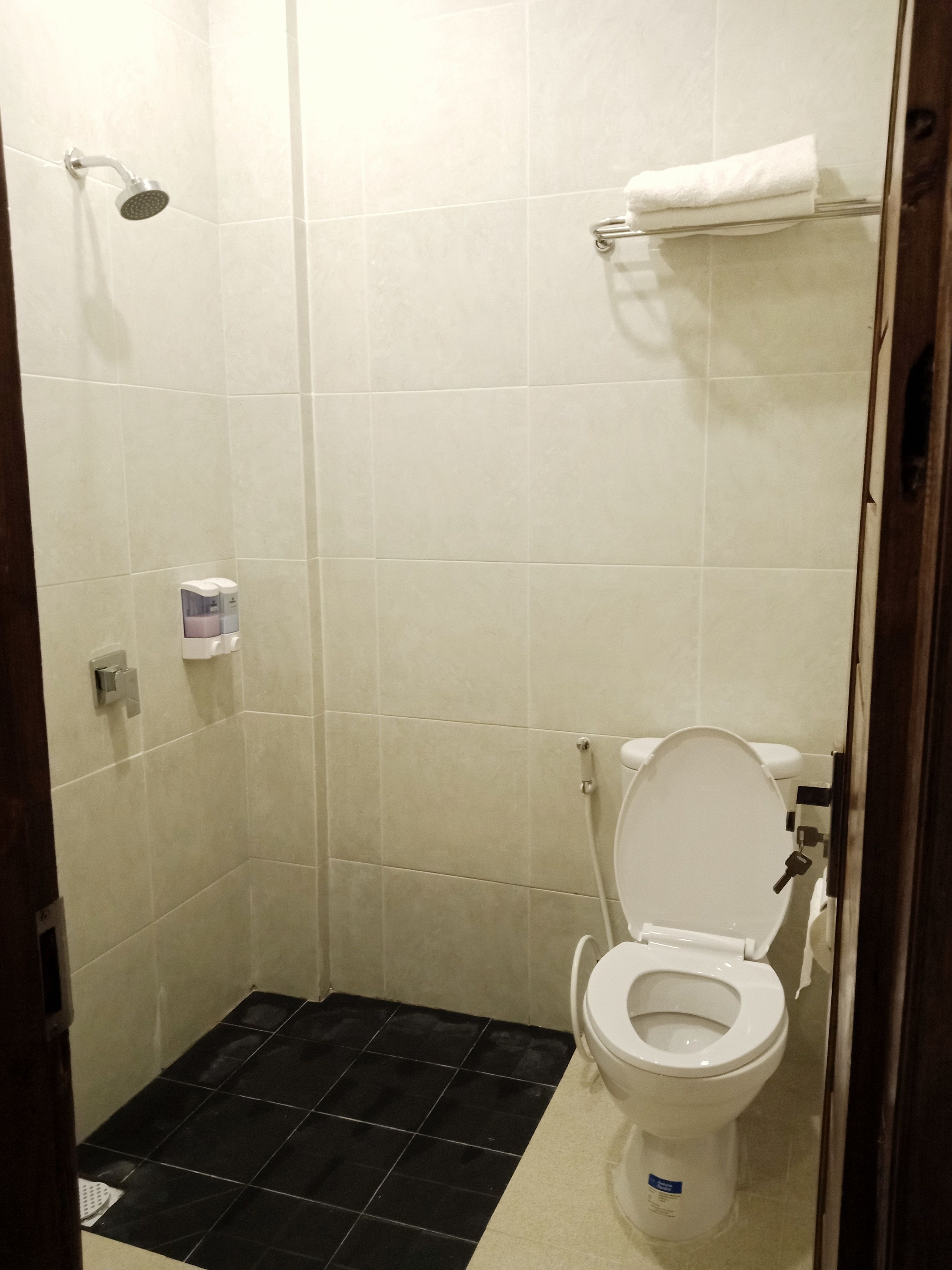 A small, tiled bathroom with a shower, toilet, and a towel rack.