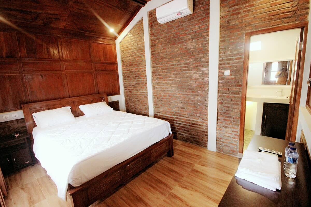 A wooden bed in a room with a brick wall and a wooden ceiling.