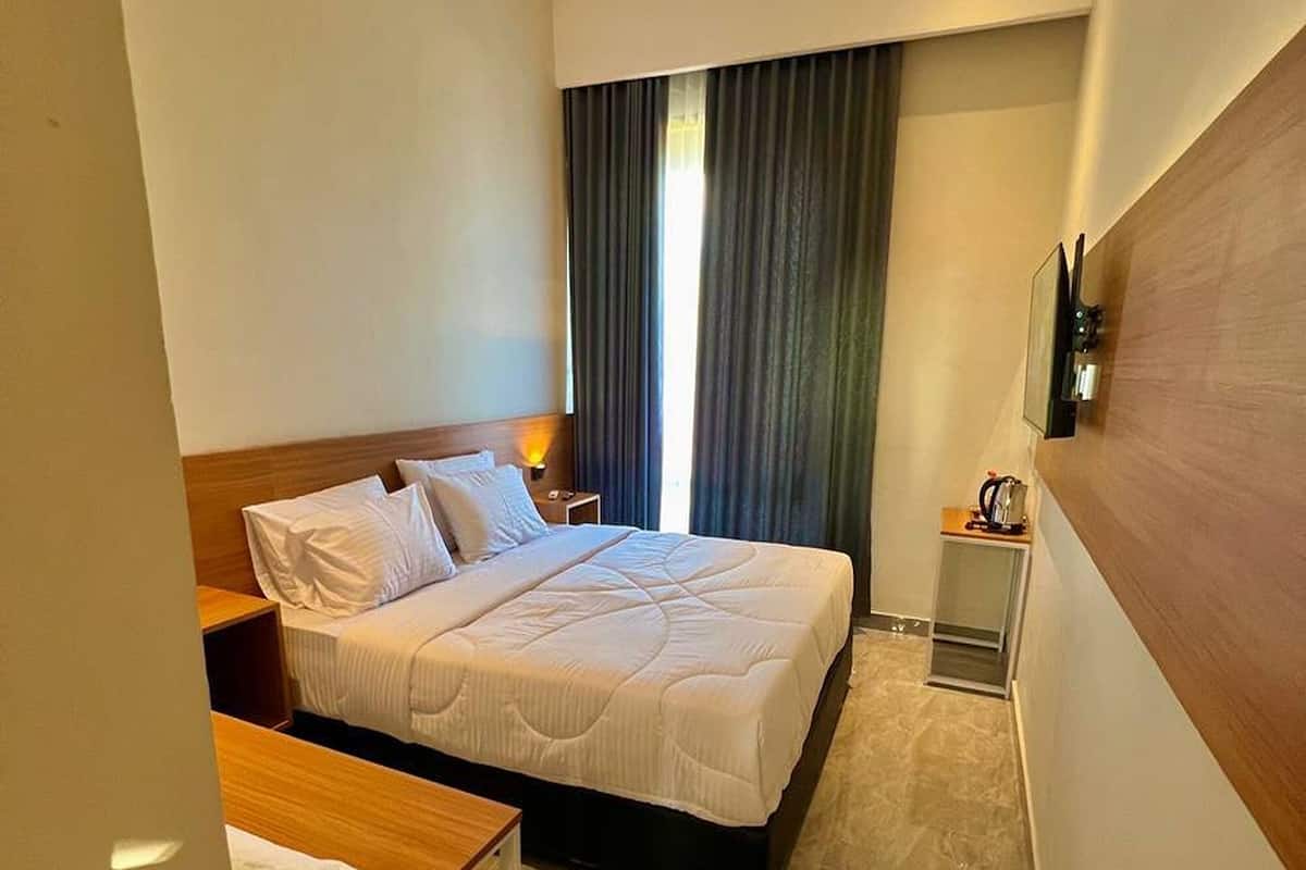 A hotel room with a bed, a desk, a chair, a TV, and a window with curtains.