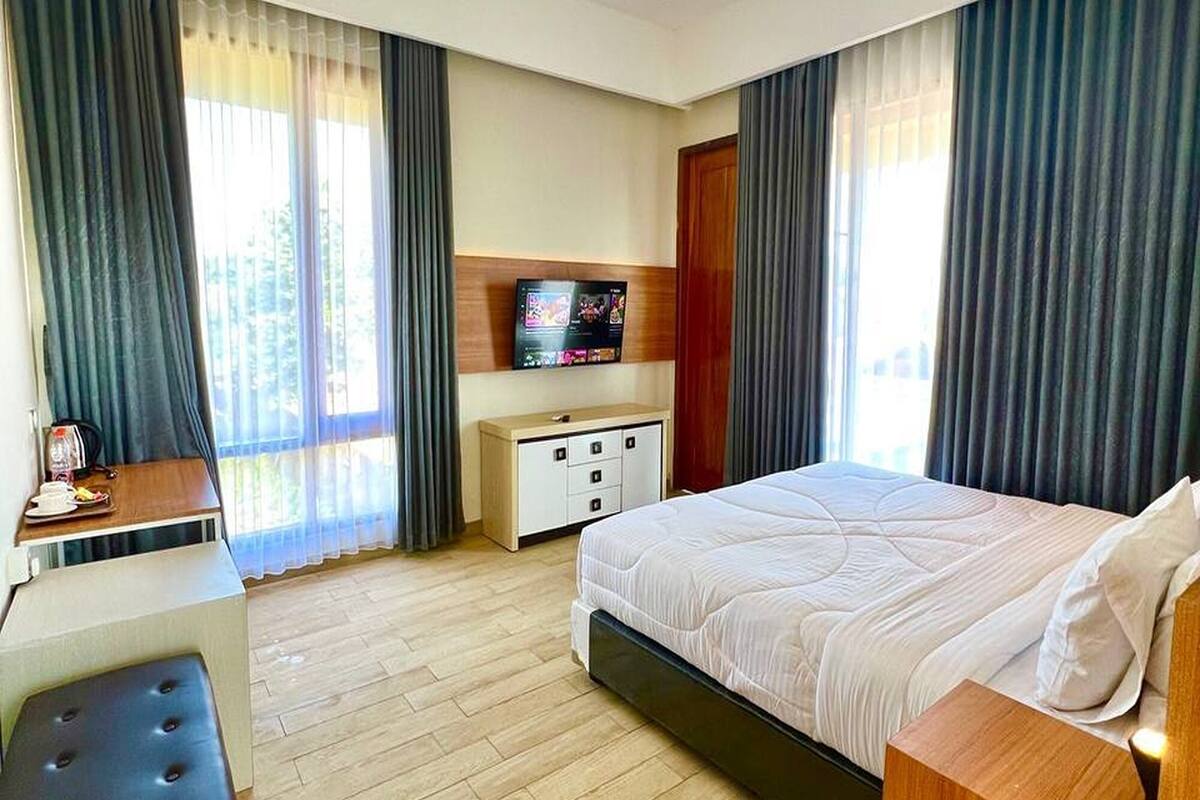 A hotel room with a bed, a desk, a television, and a wooden floor.