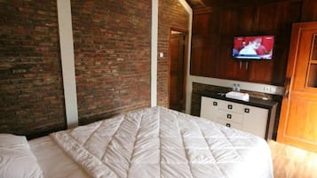 Una habitación de hotel con pared de ladrillo, una cama con colcha, un armario de madera y un televisor fijado a la pared.