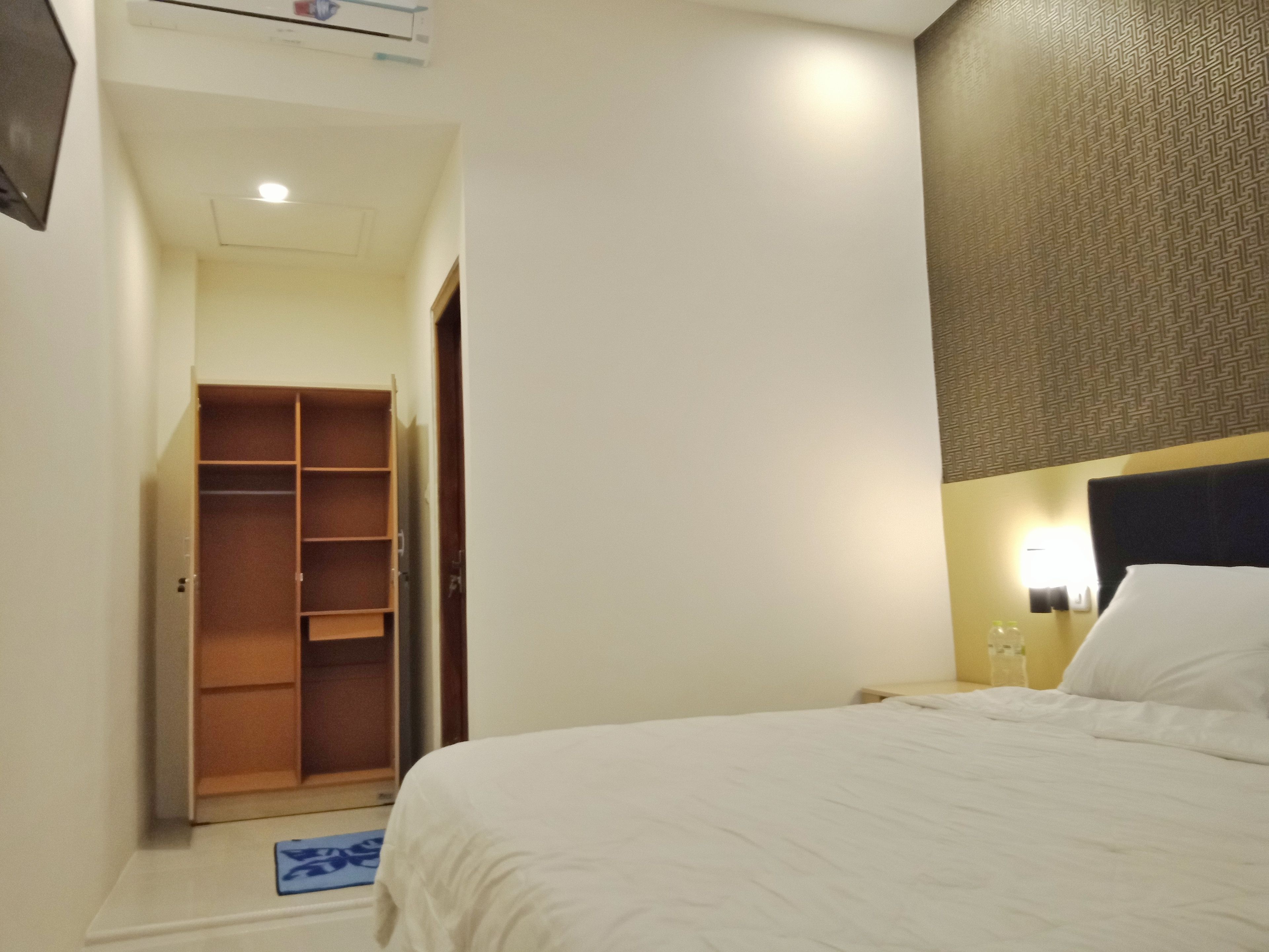 Una habitación de hotel con una cama, un armario y un escritorio pequeño con una lámpara.