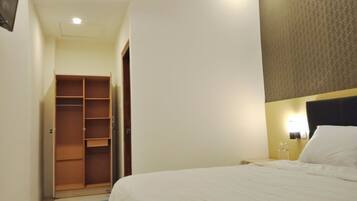 Una habitación de hotel con una cama, un armario y un escritorio pequeño con una lámpara.