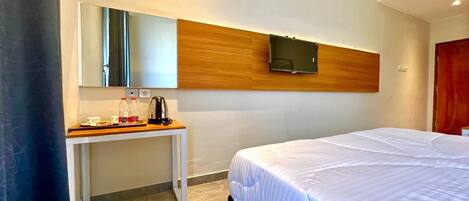 Habitación de hotel con cama, mesita de noche con lámpara, espejo y televisor de pantalla plana en la pared.
