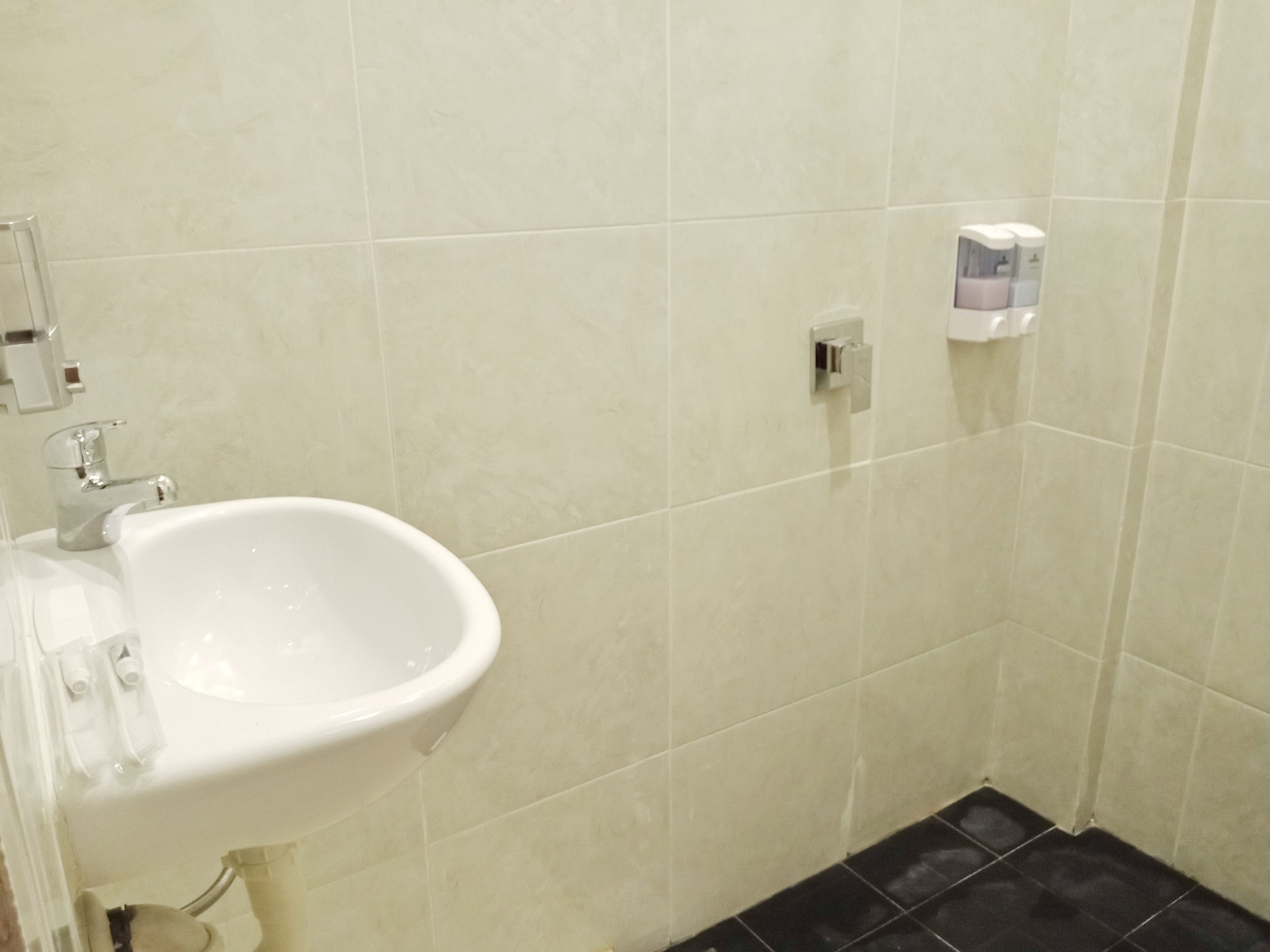 A bathroom with a white sink, a mirror, and a hand soap dispenser on the wall.