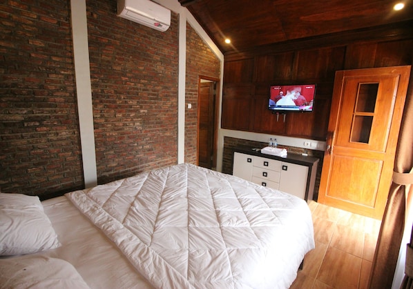 A bedroom with a brick wall, a bed, a TV mounted on the wall, and a wooden door.