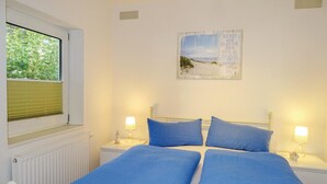 Une chambre à coucher avec un lit double, deux tables de chevet avec des lampes, une fenêtre avec des stores et un tableau accroché au mur.
