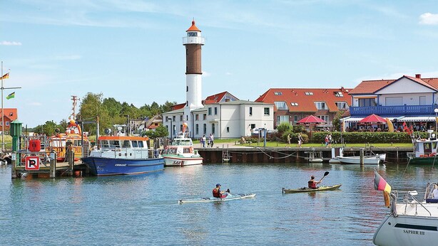 Un port avec des bateaux, un phare et des bâtiments aux toits rouges.