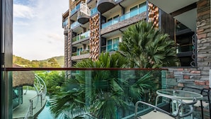 Un hotel moderno con un balcón de cristal que da a una zona de piscina, rodeado de exuberante vegetación y un paisaje montañoso.
