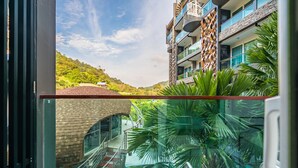 Un hotel moderno con un balcón de vidrio, una piscina y vistas a una ladera verde exuberante.