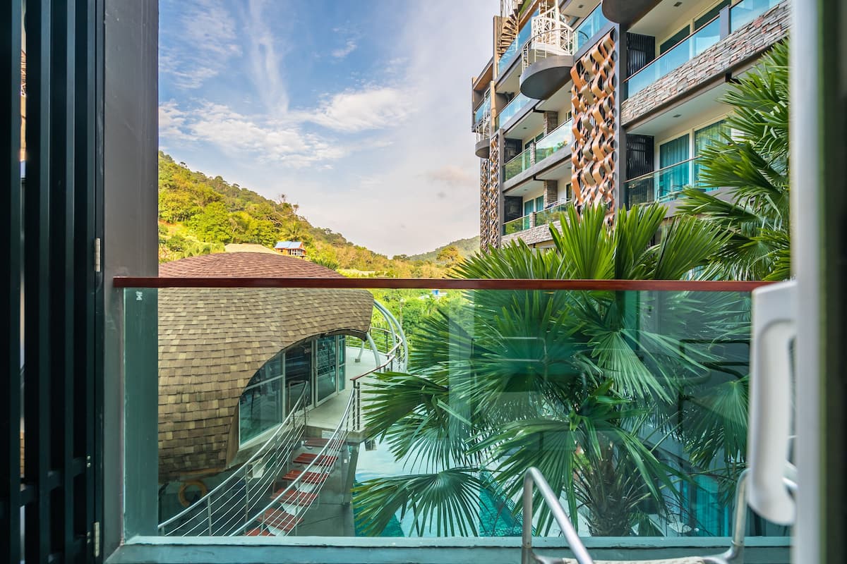 Un hôtel moderne doté d’un balcon en verre, d’une piscine et offrant une vue sur une colline verdoyante.