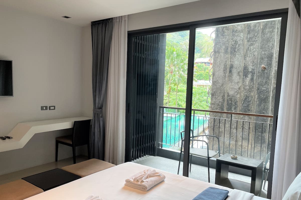 Une chambre d’hôtel équipée d’un lit, d’un bureau, d’une chaise, d’une télévision et d’un balcon donnant sur la piscine.
