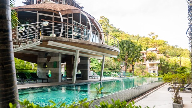 Una piscina con fondo de cristal, rodeada de sillas de descanso y un edificio con balcón.