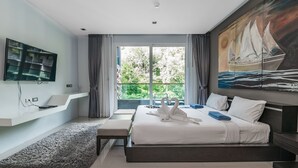 Una habitación de hotel moderna con una cama grande, un televisor de pantalla plana en la pared, un cuadro de un velero y vistas a zonas verdes por la ventana.