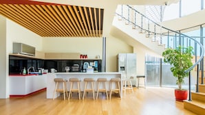 A modern kitchen with a central island, bar stools, and a staircase with a glass railing. - Chen Feng Homestay (Magong)
