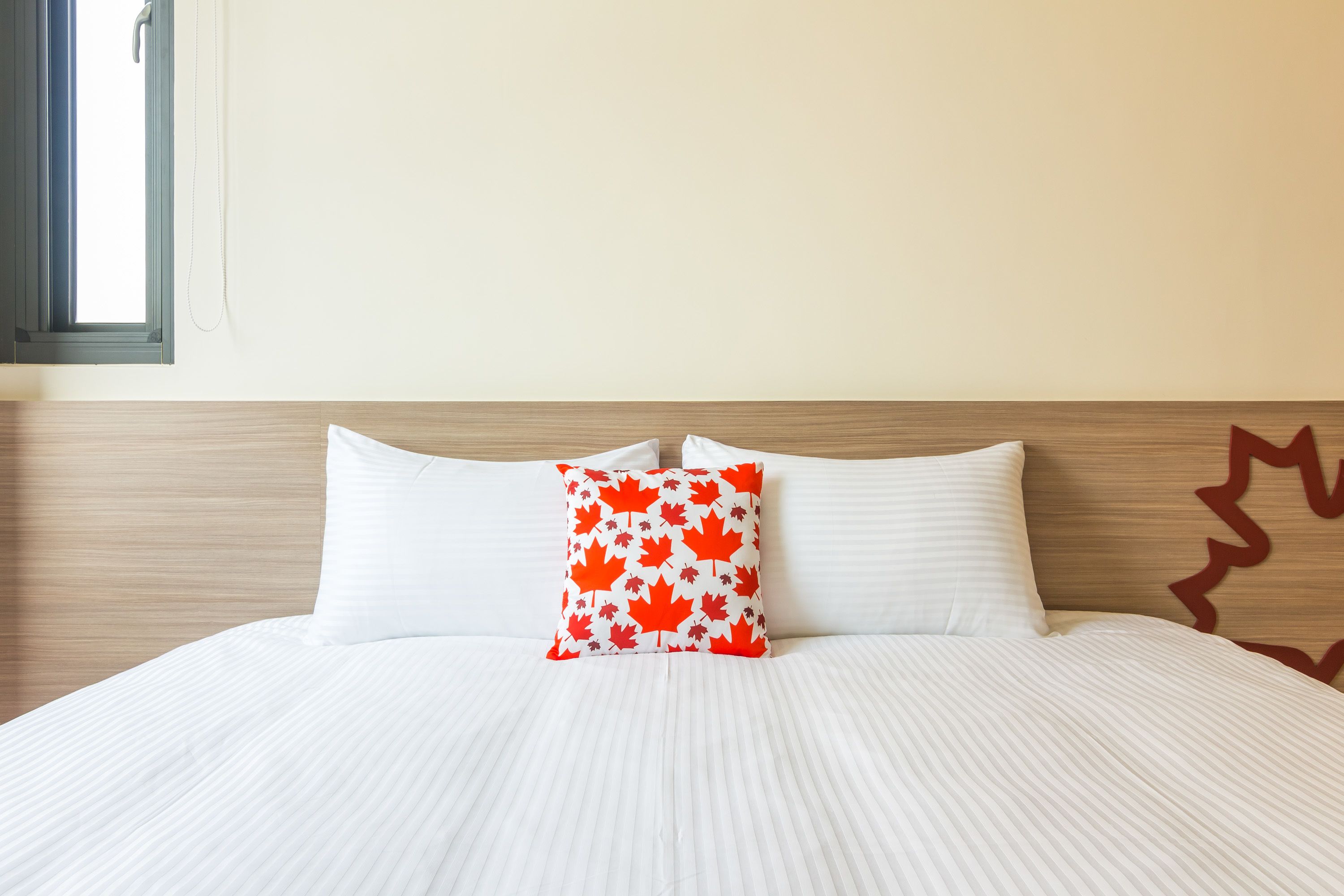 A neatly made bed with white bedding and a single red and white maple leaf pillow.