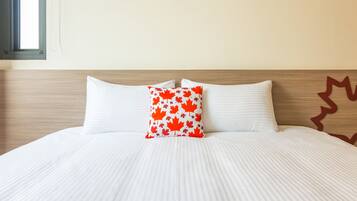 A neatly made bed with white bedding and a single red and white maple leaf pillow.