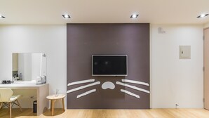 A modern room with a flat-screen TV mounted on a wall, a small round table with a candle, a chair, and a desk with a mirror and coffee maker. - Chen Feng Homestay (Magong)