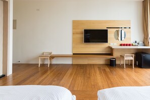 A hotel room with a wooden floor, a bed, a desk, a chair, a TV mounted on a wooden wall, a trash bin, and a minibar. - Chen Feng Homestay (Magong)
