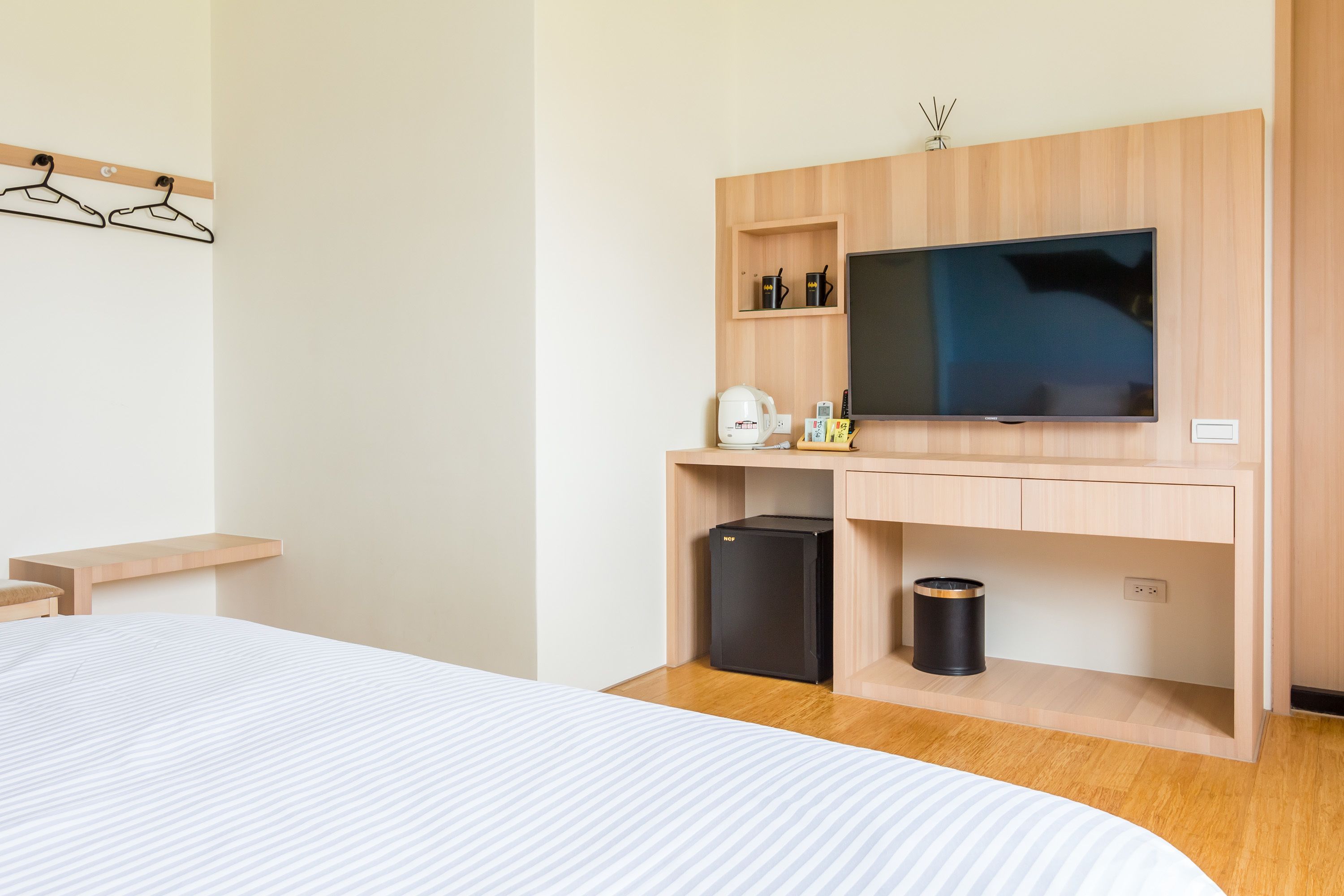 Een moderne hotelkamer met een bed, een houten bureau met een flatscreen televisie, een koffiezetapparaat en een prullenbak.