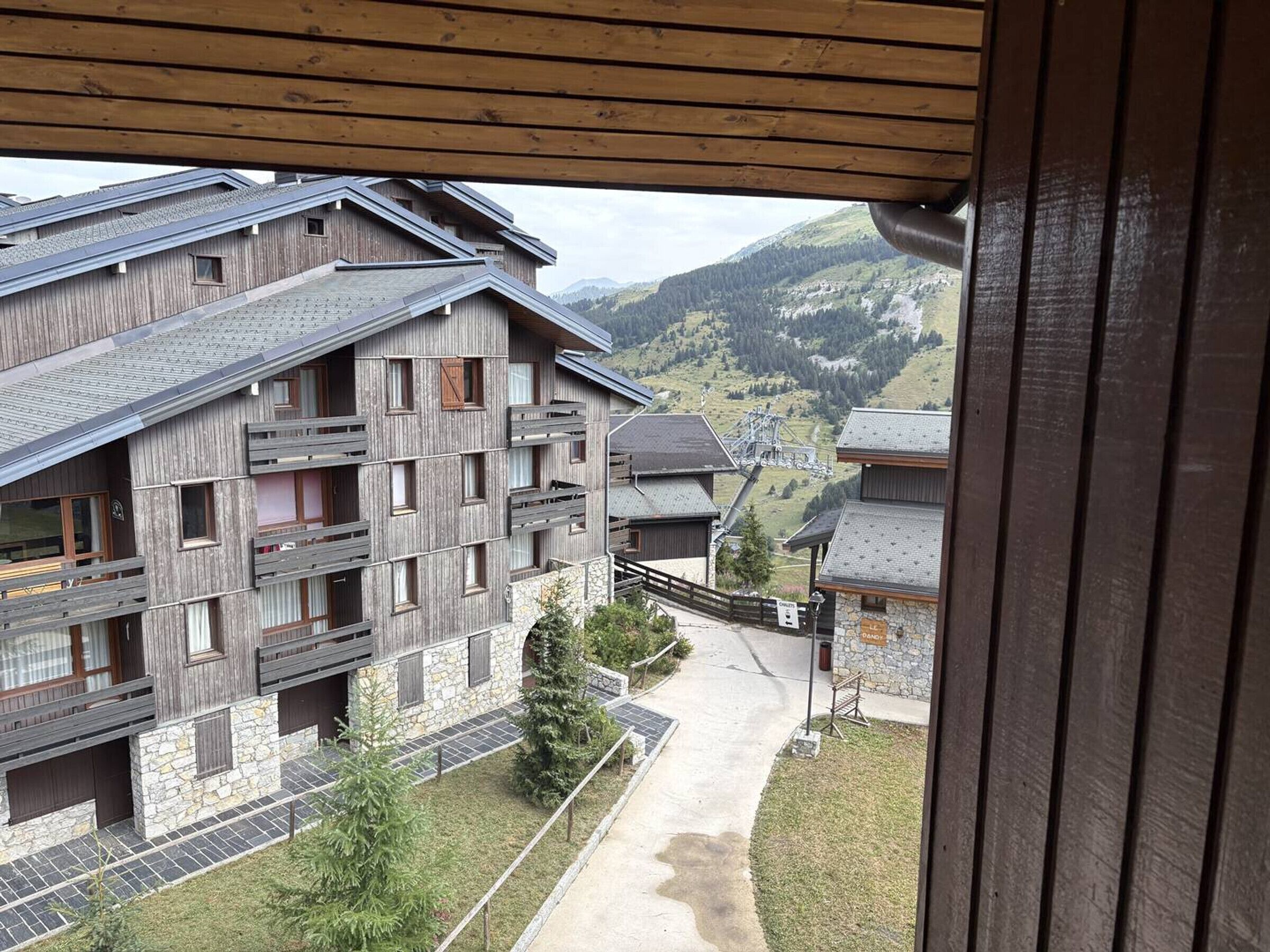 A wooden building with multiple balconies and a stone facade, overlooking a mountainous landscape.