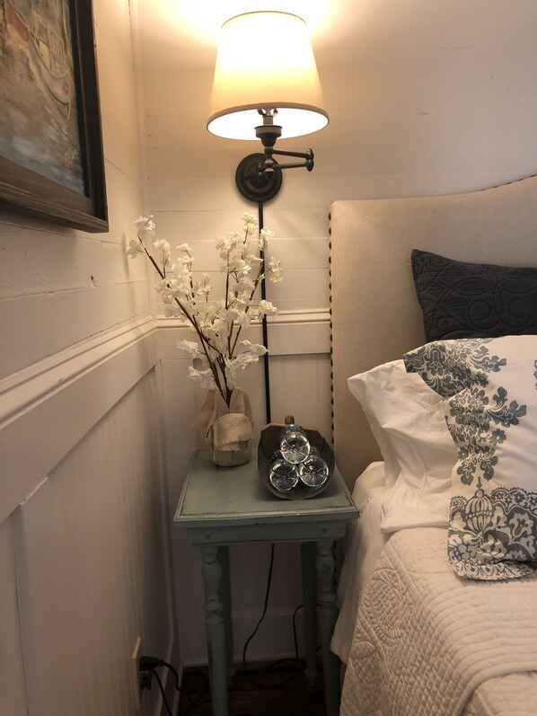A bedroom with a bed, a bedside table with a lamp, and a wall-mounted shelf with decorative items. - Old Kelleytown General Store (McDonough)