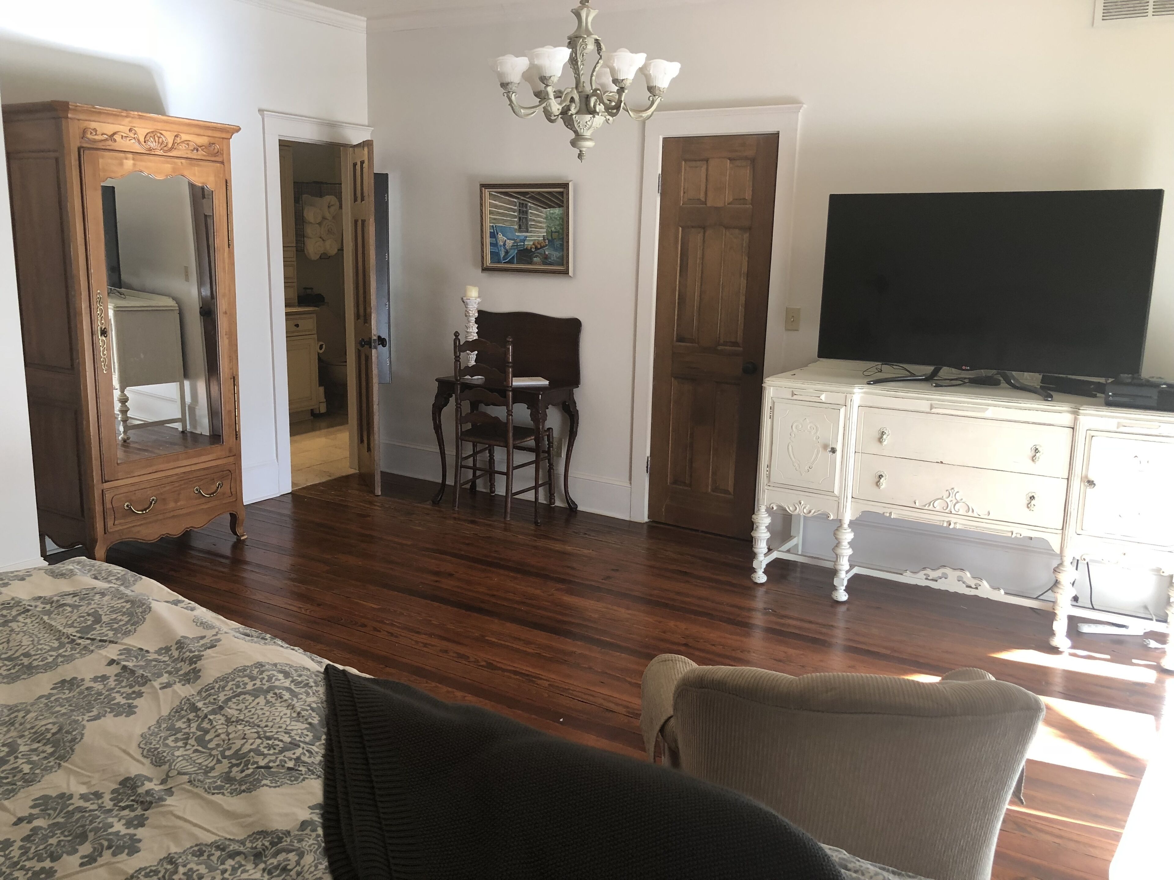 A room with a wooden floor, a bed with a patterned bedspread, a dresser with a television, and a chair.