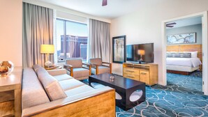Hotellihuone, jossa on sohva, nojatuoleja, televisio, sänky ja näkymä kaupungin ylle.