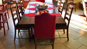 A dining area with a long wooden table, red chairs, and a central red rug.