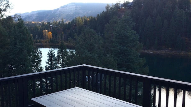 A wooden deck overlooking a lake with dense forest and mountains in the background.