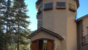A two-story building with a stone foundation and a beige exterior. There are three windows on the second floor and a wooden door on the ground floor.