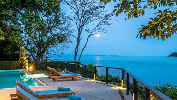 Área de piscina com espreguiçadeiras e vista para o mar.