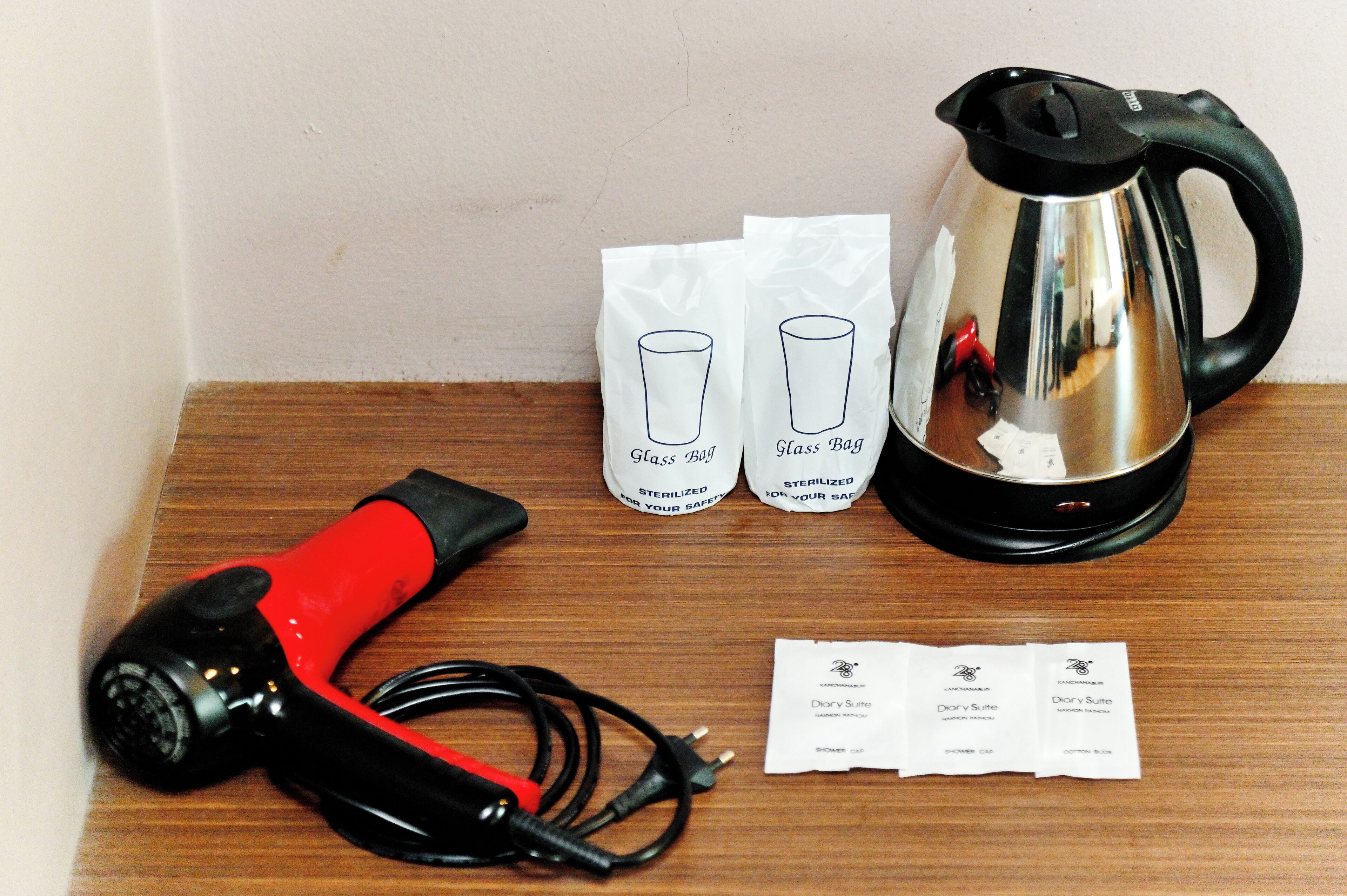 A kettle, two glass bags, a hairdryer, and a set of toiletries on a wooden surface.