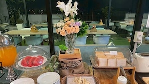 A breakfast buffet with various food items, a vase of flowers, and a view of the outdoor seating area. - Diary Suite (Nakhon Pathom)