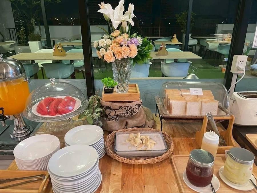 A breakfast buffet with various food items, a vase of flowers, and a view of the outdoor seating area.