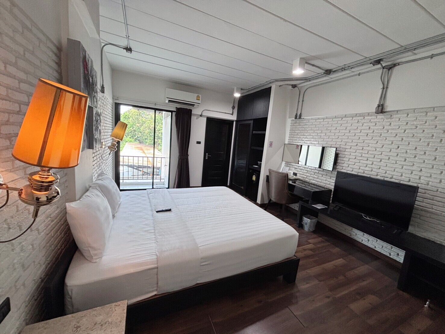 Habitación de hotel con cama, escritorio, televisión, lámpara y pared de ladrillo.