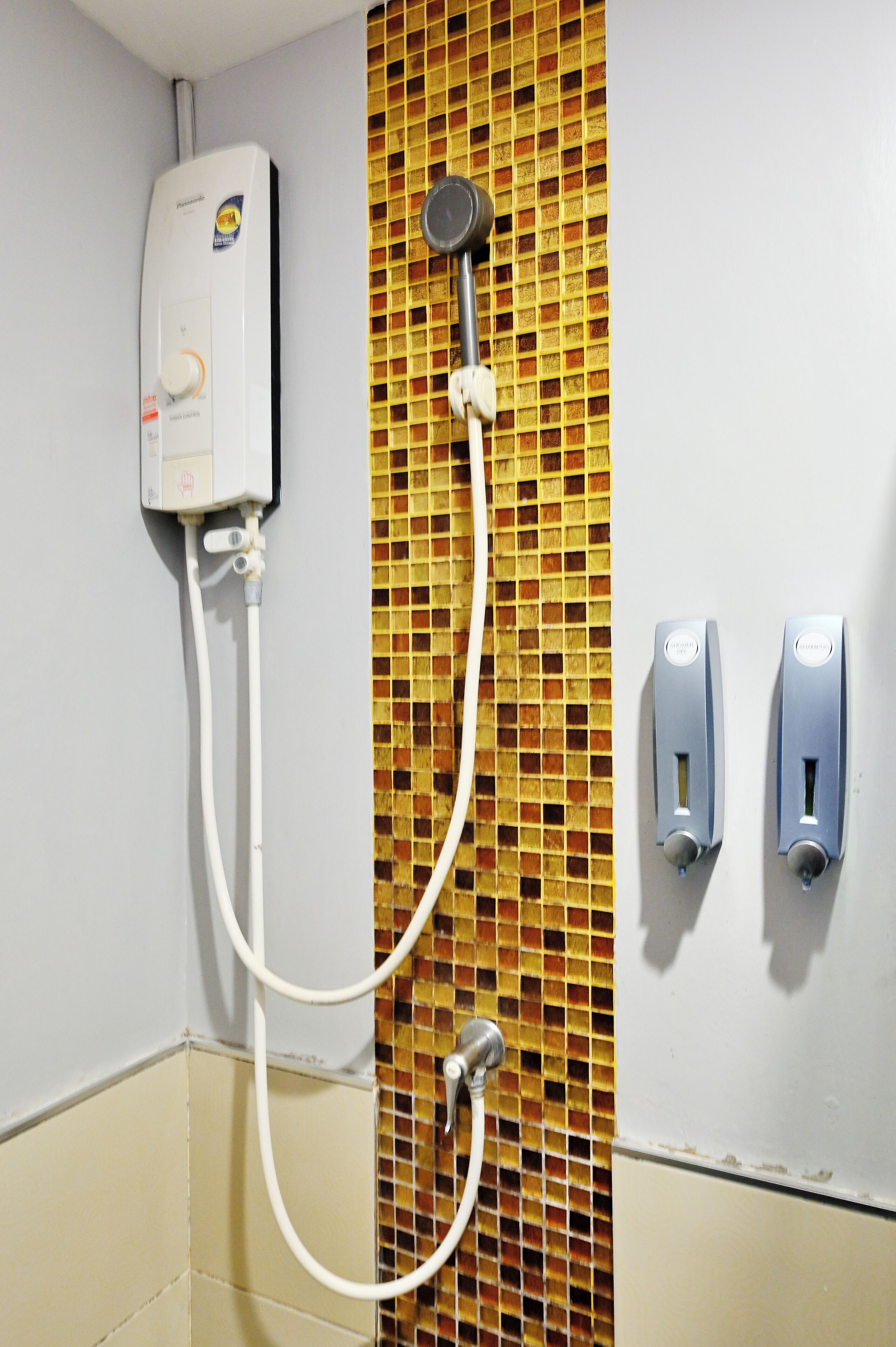 A bathroom with a shower, a wall-mounted heater, and two soap dispensers.