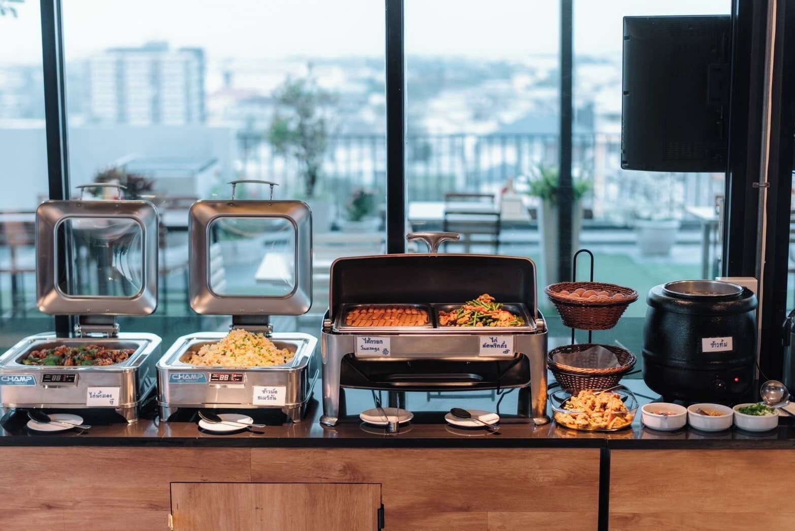 A buffet setup with various food containers and baskets, a television, and a view of buildings through large windows.