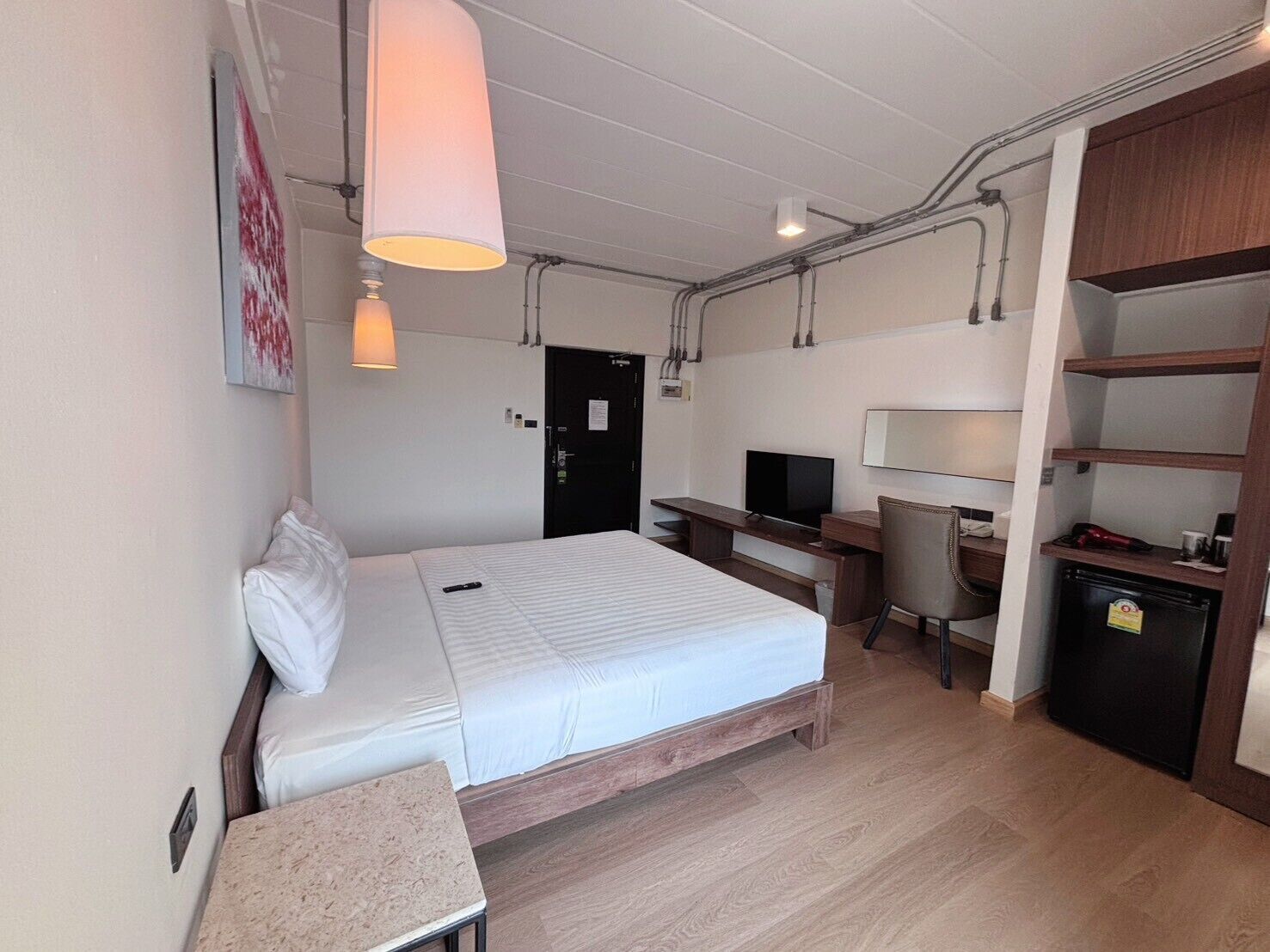 A hotel room with a bed, desk, chair, TV, and a small kitchenette.