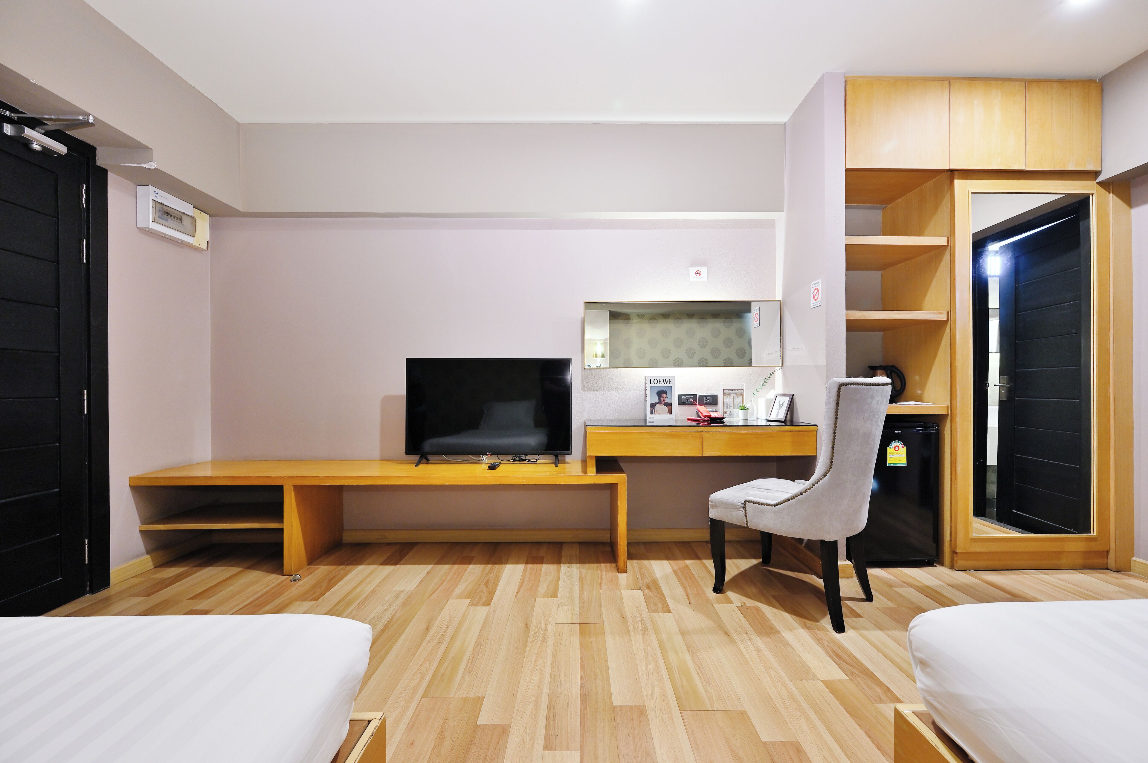 A hotel room with a wooden desk, a television, a chair, a bed, and a wardrobe.