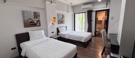 A hotel room with two beds, a desk, a chair, an air conditioning unit, and artwork on the walls.