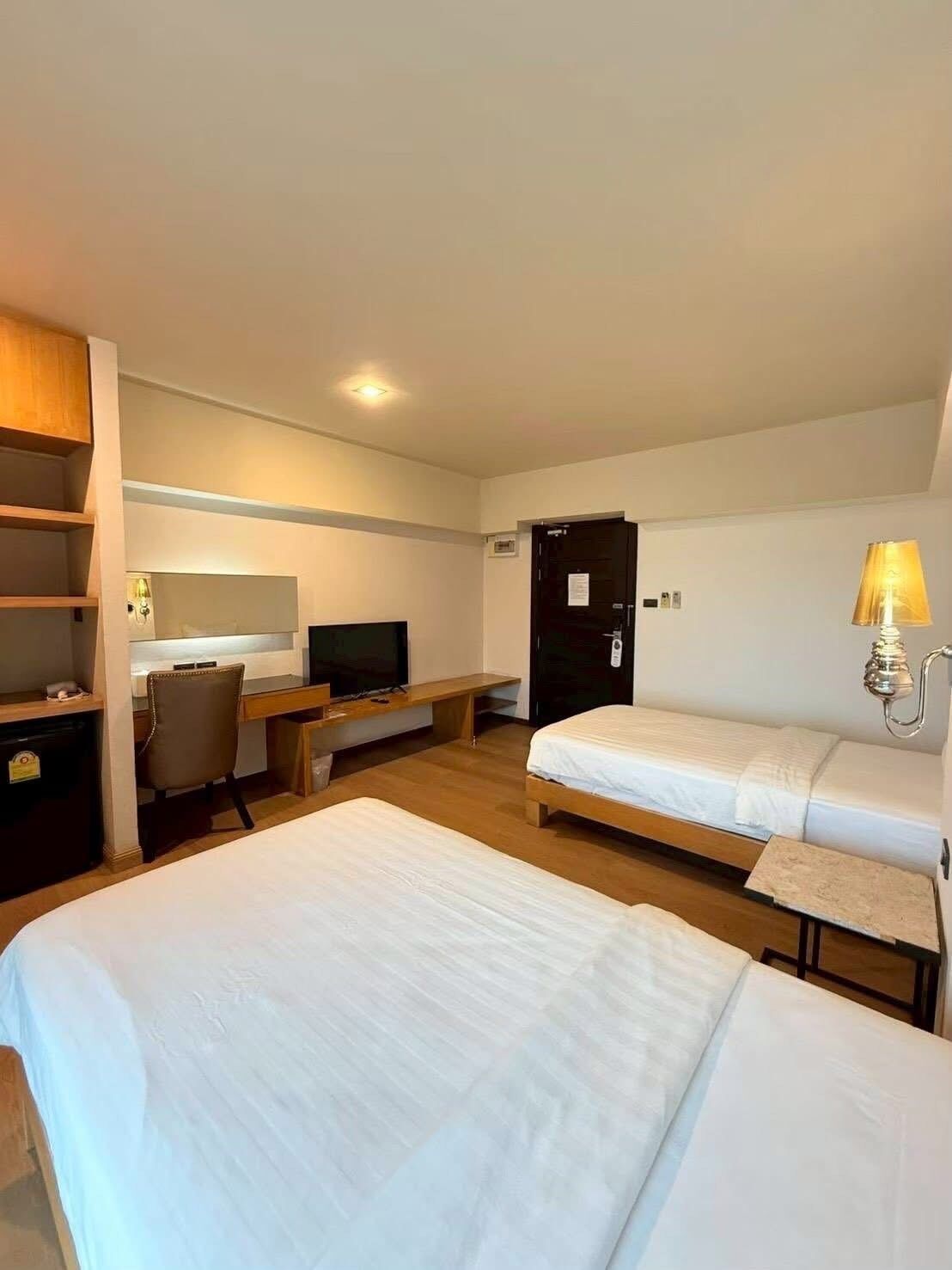 Una habitación de hotel con dos camas, un escritorio con una silla, un televisor y una puerta.