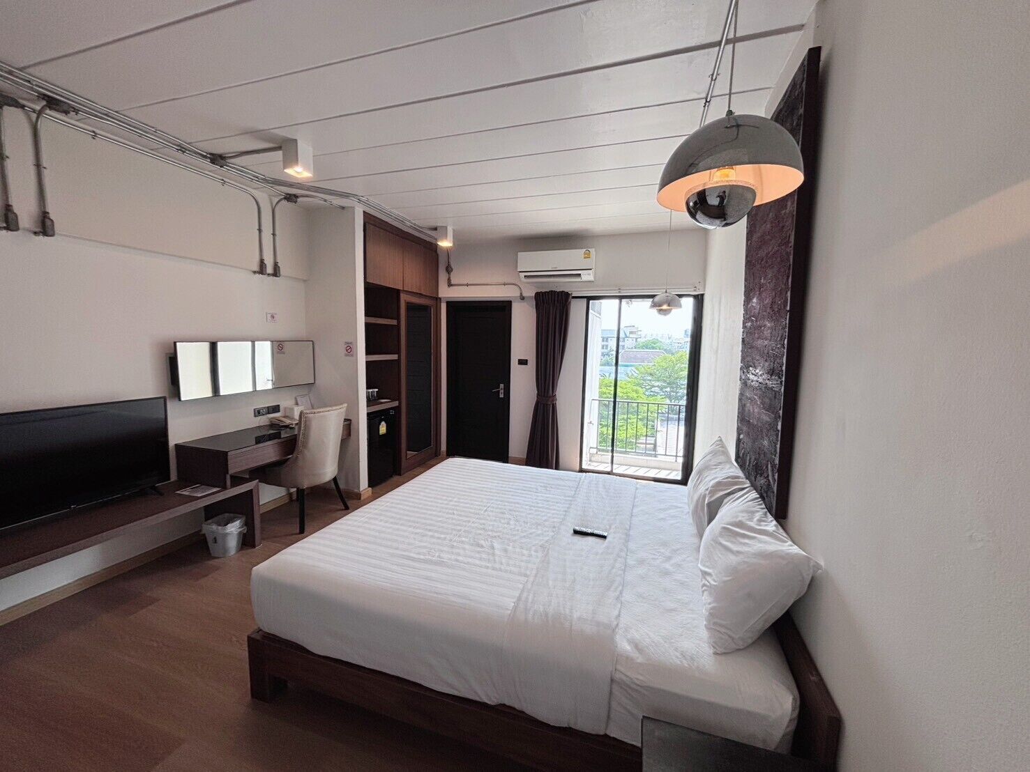 Una habitación de hotel moderna con una cama grande, un escritorio, un televisor y un balcón con vistas.