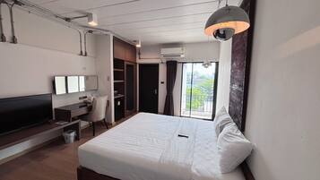 Una habitación de hotel moderna con una cama grande, un escritorio, un televisor y un balcón con vistas.