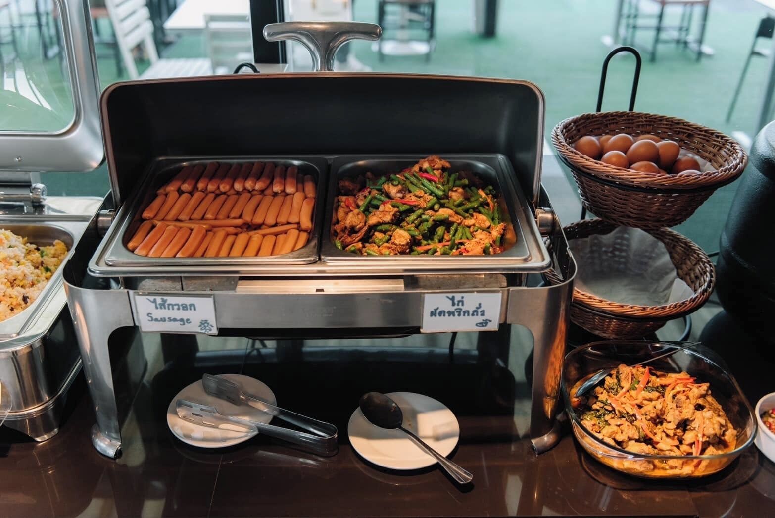 A buffet with labeled containers of hot dogs and a mixed vegetable dish.