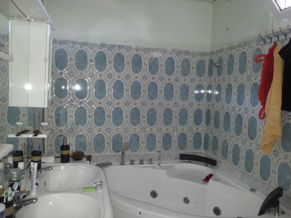 A bathroom with a large bathtub, a sink, and a mirror. There are toiletries on the sink and a towel rack with towels.