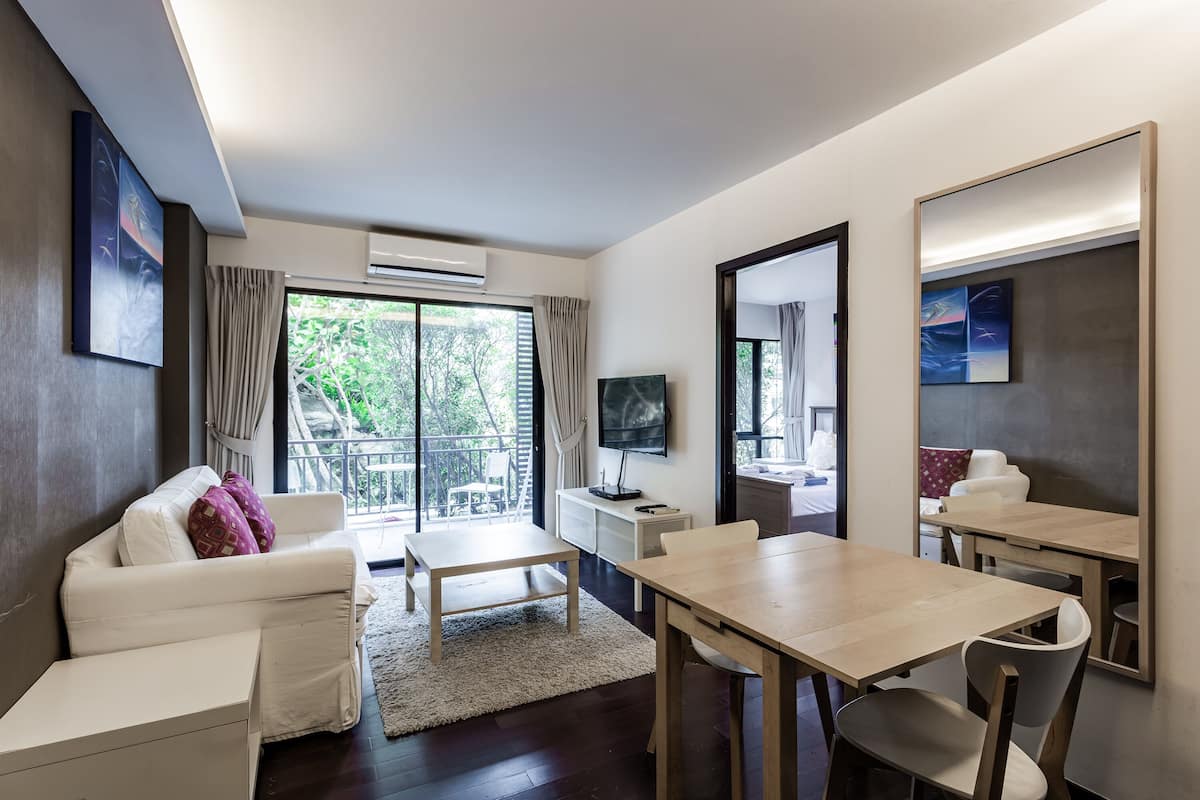 A modern room with a sofa, a dining table, a TV, and a large window.
