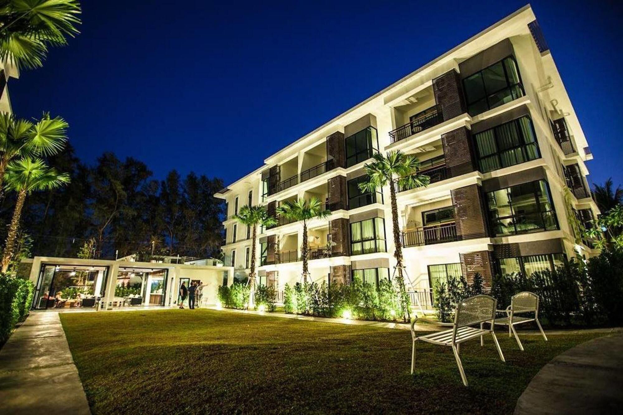 A multi-story hotel with balconies, a well-maintained lawn, and palm trees.